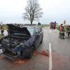 Einsatzkräfte der Feuerwehr stehen neben einem beschädigten Auto an der Unfallstelle.