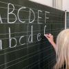Eine Grundschullehrerin schreibt die ersten Buchstaben des Alphabets auf eine Schultafel in einem Klassenzimmer.