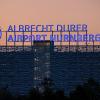 Der Schriftzug «Albrecht Dürer Airport Nürnberg» leuchtet auf dem Dach eines Parkhauses am Flughafen am Abend.
