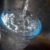 Leitungswasser fließt in ein Glas, das in einem Spülbecken steht.