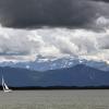 Ein Segelboot ist auf dem Starnberger See unterwegs während Gewitterwolken über die Alpen ziehen.
