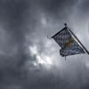 Eine Bayernfahne weht vor dichten Regenwolken im Wind.