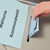 Eine Person steckt ihren Stimmzettel in eine Wahlurne mit der Aufschrift «Wahlurne Kommunalwahl».