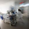 Eine Pflegerin fährt eine Intensivpatientin in einem Krankenbett durch einen Gang einer Klinik.