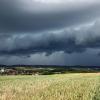 Eine Gewitterzelle mit dunklen Wolken baut sich am Himmel und hinter Feldern nahe Heilbronn auf.