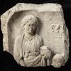 Dieses 374 kg schwere Fragment eines Grabdenkmals aus Augusta Vindelicum besteht aus Kalk. Das Relief zeigt die charakteristische Bekleidung einer römischen Frau: gegürtete Tunika und palla (Mantel). 