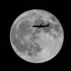 Ein Flugzeug fliegt an einem großen Vollmond vorbei.