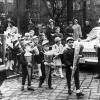 Ein Schülerlotse mit Kelle hat Autos auf der Straße vor der Schule angehalten, damit Schulanfänger mit ihren Schultüten unbesorgt von dem Verkehr über die Straße gelangen können. Das Bild stammt aus dem Jahr 1963.