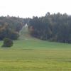 Der Solarpark käme unterhalb des Waldes und der Auffahrt auf der kräftig-grünen Wiese zu stehen. Oben ist die Kalvarienberg-Kapelle zu sehen, das Anwesen selbst ist rechts der Auffahrt vom Wald verdeckt, die Erhebung ganz rechts ist der Schlossberg, der dem Bebauungsplan den Namen gibt.