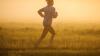 Eine Frau joggt am Morgen bei aufgehender Sonne. Am Boden hat sich Nebel gebildet.