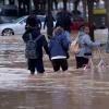 Menschen kämpfen sich in Valencia durch überflutete Straßen. 