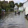 Um kurz nach 5 Uhr, am Tag der Deutschen Einheit, ist die Mindel in Jettingen (Landkreis Günzburg) übergelaufen und hat ein Wohngebiet überschwemmt. Offenbar war eine sogenannte Falle am Wasserkraftwerk defekt. Durch den starken Regen konnte nicht mehr genügend Wasser abfließen.

Wie Einsatzleiter und Kommandant der örtlichen Feuerwehr Markus Schmucker mitteilte, stand im "Korea", wie die Einheimischen das Wohngebiet am westlichen Ortsrand von Jettingen nennen, das Wasser auf den Straßen rund 20 Zentimeter hoch, als die Einsatzkräfte kamen. Und das Wasser stieg noch weiter.
Schleuse müssen geöffnet werdenAm ehemaligen Stauffenberg-Areal zwischen Mindellauf und Mindelkanal befindet sich ein Wasserkraftwerk mit zwei großen Fallen. Bei geringer ankommender Wassermenge sind beide Fallen geschlossen, um das Wasser komplett durch die Turbine zur Stromerzeugung zu leiten. Kommt aber eine so große Wassermenge von flussaufwärts an, dass das Wasser durch den alleinigen Durchfluss durch die Turbine nicht mehr abfließen kann, müssen die Fallen geöffnet werden, um ein Überlaufen der Mindel zu verhindern.Defekt an einer der SchleusenDie zweite Falle wird geöffnet, wenn notwendig. Wie der 2. Bürgermeister von Jettingen-Scheppach Hans Reichhardt berichtet, funktioniert diese zweite Falle seit geraumer Zeit allerdings nicht. Das Gestänge ist ausgehängt. Die Regenmengen am Montag waren so stark, dass das vom Oberlauf der Mindel ankommende Wasser nicht mehr genügend abgeleitet werden konnte. Das führte zum Ansteigen und schließlich zum Überlaufen der Mindel.Mindel läuft über!Das Wasser floss über mehrere Felder und überflutete schließlich das Wohngebiet bis zu einer Höhe von 1,20 Metern. Wie Reichhardt, der selbst ein Wasserkraftwerk betreibt, weiter ausführt, hatten Anwohner und die Gemeinde die Kraftwerksbetreiberin, die nicht im Landkreis wohnt, bereits dazu aufgefordert, die defekte Falle instand zu setzen. Dies sei leider bisher nicht geschehen, mit den nun entsprechenden Konsequenzen. Letztlich wurde ein von der Gemeinde betriebener Kanal geöffnet, über den eine große Wassermenge um das Wohngebiet herum abgeleitet werden kann.Große Schäden in PrivathäusernDie Familie Wolfmiller wohnt im Hammerschmiedweg und wurde vom Nachbarn gegen 6 Uhr angerufen und auf das Wasser aufmerksam gemacht. Wie der Vater sichtlich mitgenommen erklärt, hatte er dann mit einem Wassersauger im Keller das bereits dort angesammelte Wasser abgesaugt, als er plötzlich in einem Nebenraum ein Rauschen wahrnahm. Beim Nachschauen konnte er feststellen, dass dort die Bodenplatte des betonierten Kellers aufriss und das Wasser den Keller flutete. Neben Waschmaschine, Trockner und zwei Gefriertruhen ist auch der Speicher der Solaranlage im Keller. Alle Gerätschaften werden wohl komplett beschädigt worden sein.80 Kräfte im EinsatzZwischenzeitlich hatte der Einsatzleiter Schmucker u.a. noch die Feuerwehren Scheppach und Burgau nachalarmieren lassen. Insgesamt waren rund 80 Feuerwehrkräfte im Einsatz. Sie halfen mit rund 20 Tauch- und Tragkraftpumpen den Anwohnern beim vorsichtigen Auspumpen der Räumlichkeiten. Hier mussten die Einsatzkräfte aufpassen: Wenn der Wasserspiegel außen noch zu hoch ist, der Keller aber komplett leer gepumpt wird, wirkt ein großer Druck auf die Außenwände und die Bodenplatte eines Gebäudes. Das kann zu großen Schäden führen.Noch nie in diesem Ausmaß
Monika Wiesbauer, in deren Keller ebenfalls Wasser stand, zeigte ihren Garten. Dort hatte sie  noch am Sonntag Holz aufgestapelt und Blumen gerichtet. Nun steht dort das Wasser mehrere Zentimeter hoch. Die 68-Jährige wohnt dort seit 1958 und hat schon einige Male miterlebt, wie das Wasser aus dem Boden in den Keller gedrückt wurde. Dass es aber von oben in den Keller läuft und noch dazu in diesem Ausmaß, das gab es noch nie. Sie wurde gegen 6.30 Uhr von ihrem Nachbarn geweckt mit den Worten "Monika mach auf, da kommt 's Wasser." Doch viel dagegen tun konnte sie nicht. Hochwassergebiet ausgewiesenAuf die betroffenen Anwohner kommt eine schwere Zeit zu. Das Gebiet ist als Hochwassergebiet ausgewiesen. Daher ist es nicht möglich, ihre Häuser gegen solche Schäden zu versichern. Zudem müssen sie nun versuchen, die wassergetränkten Wände wieder trocken zu bekommen, was bei den aktuellen und weiter steigenden Energiekosten nochmals eine große Herausforderung darstellt. Ganz abgesehen von den beschädigten Gerätschaften und Heizungsanlagen.