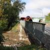 Um kurz nach 5 Uhr, am Tag der Deutschen Einheit, ist die Mindel in Jettingen (Landkreis Günzburg) übergelaufen und hat ein Wohngebiet überschwemmt. Offenbar war eine sogenannte Falle am Wasserkraftwerk defekt. Durch den starken Regen konnte nicht mehr genügend Wasser abfließen.

Wie Einsatzleiter und Kommandant der örtlichen Feuerwehr Markus Schmucker mitteilte, stand im "Korea", wie die Einheimischen das Wohngebiet am westlichen Ortsrand von Jettingen nennen, das Wasser auf den Straßen rund 20 Zentimeter hoch, als die Einsatzkräfte kamen. Und das Wasser stieg noch weiter.
Schleuse müssen geöffnet werdenAm ehemaligen Stauffenberg-Areal zwischen Mindellauf und Mindelkanal befindet sich ein Wasserkraftwerk mit zwei großen Fallen. Bei geringer ankommender Wassermenge sind beide Fallen geschlossen, um das Wasser komplett durch die Turbine zur Stromerzeugung zu leiten. Kommt aber eine so große Wassermenge von flussaufwärts an, dass das Wasser durch den alleinigen Durchfluss durch die Turbine nicht mehr abfließen kann, müssen die Fallen geöffnet werden, um ein Überlaufen der Mindel zu verhindern.Defekt an einer der SchleusenDie zweite Falle wird geöffnet, wenn notwendig. Wie der 2. Bürgermeister von Jettingen-Scheppach Hans Reichhardt berichtet, funktioniert diese zweite Falle seit geraumer Zeit allerdings nicht. Das Gestänge ist ausgehängt. Die Regenmengen am Montag waren so stark, dass das vom Oberlauf der Mindel ankommende Wasser nicht mehr genügend abgeleitet werden konnte. Das führte zum Ansteigen und schließlich zum Überlaufen der Mindel.Mindel läuft über!Das Wasser floss über mehrere Felder und überflutete schließlich das Wohngebiet bis zu einer Höhe von 1,20 Metern. Wie Reichhardt, der selbst ein Wasserkraftwerk betreibt, weiter ausführt, hatten Anwohner und die Gemeinde die Kraftwerksbetreiberin, die nicht im Landkreis wohnt, bereits dazu aufgefordert, die defekte Falle instand zu setzen. Dies sei leider bisher nicht geschehen, mit den nun entsprechenden Konsequenzen. Letztlich wurde ein von der Gemeinde betriebener Kanal geöffnet, über den eine große Wassermenge um das Wohngebiet herum abgeleitet werden kann.Große Schäden in PrivathäusernDie Familie Wolfmiller wohnt im Hammerschmiedweg und wurde vom Nachbarn gegen 6 Uhr angerufen und auf das Wasser aufmerksam gemacht. Wie der Vater sichtlich mitgenommen erklärt, hatte er dann mit einem Wassersauger im Keller das bereits dort angesammelte Wasser abgesaugt, als er plötzlich in einem Nebenraum ein Rauschen wahrnahm. Beim Nachschauen konnte er feststellen, dass dort die Bodenplatte des betonierten Kellers aufriss und das Wasser den Keller flutete. Neben Waschmaschine, Trockner und zwei Gefriertruhen ist auch der Speicher der Solaranlage im Keller. Alle Gerätschaften werden wohl komplett beschädigt worden sein.80 Kräfte im EinsatzZwischenzeitlich hatte der Einsatzleiter Schmucker u.a. noch die Feuerwehren Scheppach und Burgau nachalarmieren lassen. Insgesamt waren rund 80 Feuerwehrkräfte im Einsatz. Sie halfen mit rund 20 Tauch- und Tragkraftpumpen den Anwohnern beim vorsichtigen Auspumpen der Räumlichkeiten. Hier mussten die Einsatzkräfte aufpassen: Wenn der Wasserspiegel außen noch zu hoch ist, der Keller aber komplett leer gepumpt wird, wirkt ein großer Druck auf die Außenwände und die Bodenplatte eines Gebäudes. Das kann zu großen Schäden führen.Noch nie in diesem Ausmaß
Monika Wiesbauer, in deren Keller ebenfalls Wasser stand, zeigte ihren Garten. Dort hatte sie  noch am Sonntag Holz aufgestapelt und Blumen gerichtet. Nun steht dort das Wasser mehrere Zentimeter hoch. Die 68-Jährige wohnt dort seit 1958 und hat schon einige Male miterlebt, wie das Wasser aus dem Boden in den Keller gedrückt wurde. Dass es aber von oben in den Keller läuft und noch dazu in diesem Ausmaß, das gab es noch nie. Sie wurde gegen 6.30 Uhr von ihrem Nachbarn geweckt mit den Worten "Monika mach auf, da kommt 's Wasser." Doch viel dagegen tun konnte sie nicht. Hochwassergebiet ausgewiesenAuf die betroffenen Anwohner kommt eine schwere Zeit zu. Das Gebiet ist als Hochwassergebiet ausgewiesen. Daher ist es nicht möglich, ihre Häuser gegen solche Schäden zu versichern. Zudem müssen sie nun versuchen, die wassergetränkten Wände wieder trocken zu bekommen, was bei den aktuellen und weiter steigenden Energiekosten nochmals eine große Herausforderung darstellt. Ganz abgesehen von den beschädigten Gerätschaften und Heizungsanlagen.