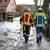 Um kurz nach 5 Uhr, am Tag der Deutschen Einheit, ist die Mindel in Jettingen (Landkreis Günzburg) übergelaufen und hat ein Wohngebiet überschwemmt. Offenbar war eine sogenannte Falle am Wasserkraftwerk defekt. Durch den starken Regen konnte nicht mehr genügend Wasser abfließen.

Wie Einsatzleiter und Kommandant der örtlichen Feuerwehr Markus Schmucker mitteilte, stand im "Korea", wie die Einheimischen das Wohngebiet am westlichen Ortsrand von Jettingen nennen, das Wasser auf den Straßen rund 20 Zentimeter hoch, als die Einsatzkräfte kamen. Und das Wasser stieg noch weiter.
Schleuse müssen geöffnet werdenAm ehemaligen Stauffenberg-Areal zwischen Mindellauf und Mindelkanal befindet sich ein Wasserkraftwerk mit zwei großen Fallen. Bei geringer ankommender Wassermenge sind beide Fallen geschlossen, um das Wasser komplett durch die Turbine zur Stromerzeugung zu leiten. Kommt aber eine so große Wassermenge von flussaufwärts an, dass das Wasser durch den alleinigen Durchfluss durch die Turbine nicht mehr abfließen kann, müssen die Fallen geöffnet werden, um ein Überlaufen der Mindel zu verhindern.Defekt an einer der SchleusenDie zweite Falle wird geöffnet, wenn notwendig. Wie der 2. Bürgermeister von Jettingen-Scheppach Hans Reichhardt berichtet, funktioniert diese zweite Falle seit geraumer Zeit allerdings nicht. Das Gestänge ist ausgehängt. Die Regenmengen am Montag waren so stark, dass das vom Oberlauf der Mindel ankommende Wasser nicht mehr genügend abgeleitet werden konnte. Das führte zum Ansteigen und schließlich zum Überlaufen der Mindel.Mindel läuft über!Das Wasser floss über mehrere Felder und überflutete schließlich das Wohngebiet bis zu einer Höhe von 1,20 Metern. Wie Reichhardt, der selbst ein Wasserkraftwerk betreibt, weiter ausführt, hatten Anwohner und die Gemeinde die Kraftwerksbetreiberin, die nicht im Landkreis wohnt, bereits dazu aufgefordert, die defekte Falle instand zu setzen. Dies sei leider bisher nicht geschehen, mit den nun entsprechenden Konsequenzen. Letztlich wurde ein von der Gemeinde betriebener Kanal geöffnet, über den eine große Wassermenge um das Wohngebiet herum abgeleitet werden kann.Große Schäden in PrivathäusernDie Familie Wolfmiller wohnt im Hammerschmiedweg und wurde vom Nachbarn gegen 6 Uhr angerufen und auf das Wasser aufmerksam gemacht. Wie der Vater sichtlich mitgenommen erklärt, hatte er dann mit einem Wassersauger im Keller das bereits dort angesammelte Wasser abgesaugt, als er plötzlich in einem Nebenraum ein Rauschen wahrnahm. Beim Nachschauen konnte er feststellen, dass dort die Bodenplatte des betonierten Kellers aufriss und das Wasser den Keller flutete. Neben Waschmaschine, Trockner und zwei Gefriertruhen ist auch der Speicher der Solaranlage im Keller. Alle Gerätschaften werden wohl komplett beschädigt worden sein.80 Kräfte im EinsatzZwischenzeitlich hatte der Einsatzleiter Schmucker u.a. noch die Feuerwehren Scheppach und Burgau nachalarmieren lassen. Insgesamt waren rund 80 Feuerwehrkräfte im Einsatz. Sie halfen mit rund 20 Tauch- und Tragkraftpumpen den Anwohnern beim vorsichtigen Auspumpen der Räumlichkeiten. Hier mussten die Einsatzkräfte aufpassen: Wenn der Wasserspiegel außen noch zu hoch ist, der Keller aber komplett leer gepumpt wird, wirkt ein großer Druck auf die Außenwände und die Bodenplatte eines Gebäudes. Das kann zu großen Schäden führen.Noch nie in diesem Ausmaß
Monika Wiesbauer, in deren Keller ebenfalls Wasser stand, zeigte ihren Garten. Dort hatte sie  noch am Sonntag Holz aufgestapelt und Blumen gerichtet. Nun steht dort das Wasser mehrere Zentimeter hoch. Die 68-Jährige wohnt dort seit 1958 und hat schon einige Male miterlebt, wie das Wasser aus dem Boden in den Keller gedrückt wurde. Dass es aber von oben in den Keller läuft und noch dazu in diesem Ausmaß, das gab es noch nie. Sie wurde gegen 6.30 Uhr von ihrem Nachbarn geweckt mit den Worten "Monika mach auf, da kommt 's Wasser." Doch viel dagegen tun konnte sie nicht. Hochwassergebiet ausgewiesenAuf die betroffenen Anwohner kommt eine schwere Zeit zu. Das Gebiet ist als Hochwassergebiet ausgewiesen. Daher ist es nicht möglich, ihre Häuser gegen solche Schäden zu versichern. Zudem müssen sie nun versuchen, die wassergetränkten Wände wieder trocken zu bekommen, was bei den aktuellen und weiter steigenden Energiekosten nochmals eine große Herausforderung darstellt. Ganz abgesehen von den beschädigten Gerätschaften und Heizungsanlagen.