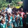 Father Joseph Sserunjogi ist umgeben von fröhlichen Schülerinnen und Schülern. Der Geistliche hat die Schule in Uganda gegründet. Ihr fließt der Erlös des Faschingsmarktes der Aktion Hoffnung am 10. Januar in Aichach zu.