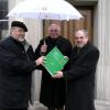 Pfarrer Manfred A. Kolberg (rechts) übernahm die Amtsgeschäfte von Pfarrer Helmut Kastner (links) und wirkt nun offiziell als Diakonie-Beauftragter im Dekanat Rügheim. Dabei wurde symbolisch eine „Mappe der ersten Stunde“ überreicht, Dekan Hartmut Gehlert hält im wörtlichen wie auch im übertragenen Sinn einen Diakonie-Schirm über die beiden.