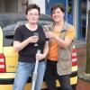 Sylvia Kaiser und Sabine Hetterich vor dem Auto, mit der Glücks-Bürste in der Hand.
