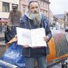 Seine Mission ist noch nicht beendet: der aus Hamburg stammende Rainer Hoffmann vor dem Fischerbrunnen am Marktheidenfelder Marktplatz. In den Händen hält er eine seiner Mappen, in denen er Unterschriften sammelt, Zeitungsausschnitte aufbewahrt und Behördenschreiben abheftet. Der 160 Kilogramm schwere Handwagen, an dem er zwei geschenkte Freiberger Nummernschilder befestigt hat, dient ihm als Transportmittel und Schlafstätte zugleich.