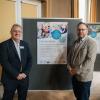 Von der Frankenklinik DRV Nordbayern: Chefarzt Dr. med. Christian Kuzman-Anton (l.) und Moritz Kaiser, Stellvertretender Kaufmännischer Leiter vor dem Poster der Frankenklinik