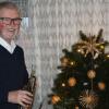 Pfarrer Rudolf Scherbaum mit seiner Trompete vor der aus Olivenholz geschnitzten Krippe aus Bethlehem
