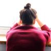 Psychische Probleme und Depressionen: Eine Frau sitzt mit Kopf in den Händen am Fenster (Symbolbild). 
