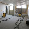 Nach der vollständigen Räumung des Neubautraktes wurden in den mit Fließen- und Linoleum-Belag versehenen Fußböden Löcher gebohrt, in die Rohre von Trocknungsgeräten eingebracht wurden. In jedem der fünf Räume sind aktuell mindestens drei Geräte im Einsatz.