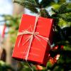Ein rotes Geschenk hängt an einem Tannenbaum im Freien.  Doppelt Geschenke gibt es für alle, die rund um Weihnachten Geburtstag haben. 