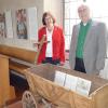 Pfarrerin Doris Schirmer-Henzler und Pfarrer Christof Henzler stehen in der Ausstellung hinter einem geschichtsträchtigen Handwagen aus dem Bauernmuseum Frensdorf.