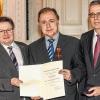 Staatssekretär Gerhard Eck (links) und der Abteilungsdirektor der Regierung von Unterfranken, Manfred Wetzel (rechts) haben Altlandrat Harald Leitherer die Ordensinsignien des Verdienstordens überreicht.