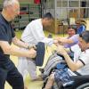 Wehr dich! Georg Müller und Horst Kohl (links) geben den gehandicapten Lebenshilfe-Mitarbeitern Ronny und Sandra Tipps zur Selbstverteidigung aus dem Rollstuhl heraus. Nach kurzer Übungsphase kann Ronny das Bein des Angreifers mit einem Schlag abwehren.
