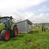 Mit dem Traktor wird die mobile Hühnerlegestation auf Kufen in ein Feld mit frischem Grün gezogen. Mit dem Traktor wird die mobile Hühnerlegestation auf Kufen in ein Feld mit frischem Grün gezogen.