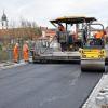 (rwe)   Heißer Dampf zog durch die Hauptstraße; als die Bauarbeiter der Firma Leonhard Weiss mit ihrer automatischen Asphaltiermaschine auf der Brücke eine Schicht nach der anderen aufzogen. Zuerst kam eine 14 Zentimeter dicke Tragschicht mit grober Körnung; danach kam der acht Zentimeter starke Binder. Als Deckschicht wurde dann der zwei Zentimeter dicke „Gussasphalt“– auch Flüsterasphalt genannt – mit einer Temperatur von 194 Grad Celsius über die gesamte Fläche in einem Guss aufgetragen. Die Arbeiter tragen dazu spezielles Schuhwerk, das ihre Füße vor der Hitze von unten schützt. Die ersten zwei Schichten kamen vom Asphaltmischwerk Schwarzenau und die letzte besondere Schicht von Bayerische-Asphalt-Mischwerke in Röthlein. Das Material wurde, um die Temperatur zu halten, in großen 26,5 Tonnen- Thermo-Muldern herangefahren und in die automatische Asphaltiermaschine gekippt. Hinter der Maschine kommt der vorverdichtete Asphalt heraus, der danach noch mit einer Straßenwalze voll verdichtet wird. In einem weiteren Schritt werden  die überstehenden Ränder zur Wasserrinne hin abgeschnitten. Damit alles richtig eingebaut und aufgetragen wird, waren von Seiten des Staatlichen Bauamts und des Architekten Büros Fachleute anwesend, die die Arbeiten beobachteten und protokollierten. Eigentlich wäre nach diesen Arbeiten der zweite von vier Straßenabschnitten fertig zum Befahren, doch noch viel Feinarbeit wie Straßenmarkierungen, Wassereinläufe, Straßenschilder und die wasserführenden Rinnen sind noch zu überprüfen oder anzulegen, bis der Verkehr wieder über diesen Straßenabschnitt fahren kann.