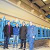 (hh)  Seit April 2011 produziert die Glöckle Montagebau GmbH am Standort Walldorf/Meiningen Spannbeton-Fertigteile. Durch eine 700 000-Euro-Investition ist diese Fertigung nun auch am Glöckle-Standort in Schwebheim möglich. Diese Erweiterung der Produktpalette mit einer Binderschalung von 62 Metern Länge ermöglicht Betonbinder für größere Spannweiten von bis zu 40 Metern. Das derzeit mögliche Stückgewicht beträgt maximal 40 Tonnen. Bereits im Dezember 2014 wurden die Vorarbeiten – Aufschneiden der Bodenplatte und Aushub der Fundamente inklusive Magerbetonschicht – für die neue Spannbetonanlage begonnen. Die Lieferung der kompletten Anlage (Schalung und Spanntechnik) erfolgte Anfang März. Nach der Montage vor kurzem konnten jetzt die ersten beiden Spannbetonbinder mit einer Länge von 30,07 Metern (Höhe 1,40 Meter) sowie einem Einzelgewicht von 24 Tonnen in Doppelbelegung gefertigt werden. Im Bild (von links) Harald Läpple, Matthias Raschke, Firmenchef Klaus Glöckle und Fabian Schleyer.