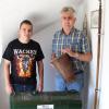 Feuerwehr-Vorsitzender Benjamin Diaz Sanchez (links) und Fred Bock, seit 1969 Aktiver in den Reihen der Wehr und seit 1998 Schriftführer, präsentieren historische Stücke der Feuerwehr, so die Motorspritze Baujahr 1934 und den jahrhundertealten Löscheimer. Rechts im Bild: die von Haus zu Haus weitergegebene Lanze der früheren Kirchenwache, die zu Gottesdienstzeiten ihre Runde im Dorf drehte.