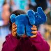 Ein Mädchen hält sich das Maskottchen des Kinderhauses Blauer Elefant vor das Gesicht.
