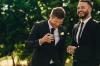 Groom and best man drinking and smiling during wedding party. Groom and groomsmen partying after wedding.