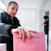 Eine Frau wirft einen Umschlag mit den Stimmzetteln in eine Wahlurne. Wen werden Sie am 15. März wählen?