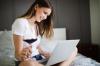 Happy lady using a laptop searching online on the bed at home