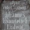Der schön verzierte Grabstein zeigt auf der Vorderseite folgende Inschrift: "Hier - ruhet in Gott. - Johannes - Evangeliest - Ludwig - Müllermeister - geb. zu Karbach - den 1. März 1794 - gest. d. 17. August 1855. Auf der Rückseite: Selig die Todten - die im Herrn - sterben, - ja spricht der Geist - Sie ruhen aus von - ihren Leiden ihre - Wercken folgen - ihnen nach.