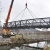 11.03.2021, Bayern, Bürgstadt: Ein Kran entfernt die neue Brücke über die Erf wieder, nachdem sich herausgestellt hat, dass einer der Aufleger nicht hoch genug ist.