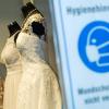 Verkaufsschlager oder Ladenhüter? Brautkleider in einem Schaufenster eines Brautmoden-Geschäfts, im Vordergrund steht ein Schild, das auf die Maskenpflicht während der Corona-Pandemie verweist (Symbolbild). Heiraten momentan im Landkreis Rhön-Grabfeld weniger Paare als sonst zu dieser Zeit und könnte das mit der Pandemie zu tun haben?