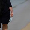 Eine Frau trägt eine medizinische Maske in der Hand bei ihrem Spaziergang am Strand. Die Menschen trauen sich wieder verstärkt, in den Urlaub zu fahren - auch weiter weg. Eine Frau trägt eine medizinische Maske in der Hand bei ihrem Spaziergang am Strand. Die Menschen trauen sich wieder verstärkt, in den Urlaub zu fahren - auch weiter weg.