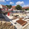 Blick auf die Baustelle am Gut Deutschhof in Schweinfurt. Die Bodenplatte für die Tiefgarage unter der Remise ist bereits fertig, im Hintergrund und halb verdeckt von einem Baum ist das alte Herrenhaus zu sehen, das noch saniert werden soll.