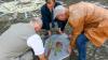 Das Denkmal am Wilhelm-Schwinn-Platz erhält seine 20. Gedenkplatte. Sie trägt das Mosaik "Versöhnung in unserer Stadt" in sich. Schulleiter Alban Schraut (von links), Stadtrat Wolfgang Roth und Bildhauer Thomas Reuter  heben die Platte an ihren Platz.