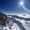 Die Sonne scheint über dem Gipfelkreuz der schneebedeckten Zugspitze.
