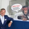 Wolfgang Grupp senior mit einem Werbeschild, auf dem der bekannte Werbe-Affe "Charly" abgebildet ist.