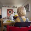 Eine Frau sitzt im Homeoffice an ihrem Laptop und telefoniert, während ihr Kind neben ihr in einem Kinderstuhl am Tisch sitzt.