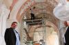 Kirchenpfleger Herbert Mahr (re.) und Pfarrer Henryk Chelskowski stehen in der vollkommen ausgeräumten und zum verhüllten Kirche. Im Hintergrund arbeitet eine Restauratorin an einem Stuckelement an der Decke.Fotos: Roger Martin