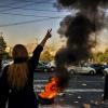 Eine Frau steht während einer Demonstration in Teheran vor einem brennenden Autoreifen und zeigt das Victory-Zeichen.