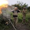 Ein ukrainischer Soldat während eines Funkgesprächs, während ein anderer Soldat 82-mm-Mörser auf russische Stellungen feuert.